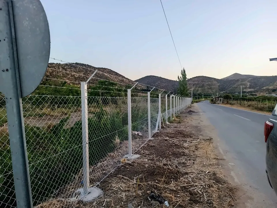 Cierro perimetral con postes y malla junto a un camino rural