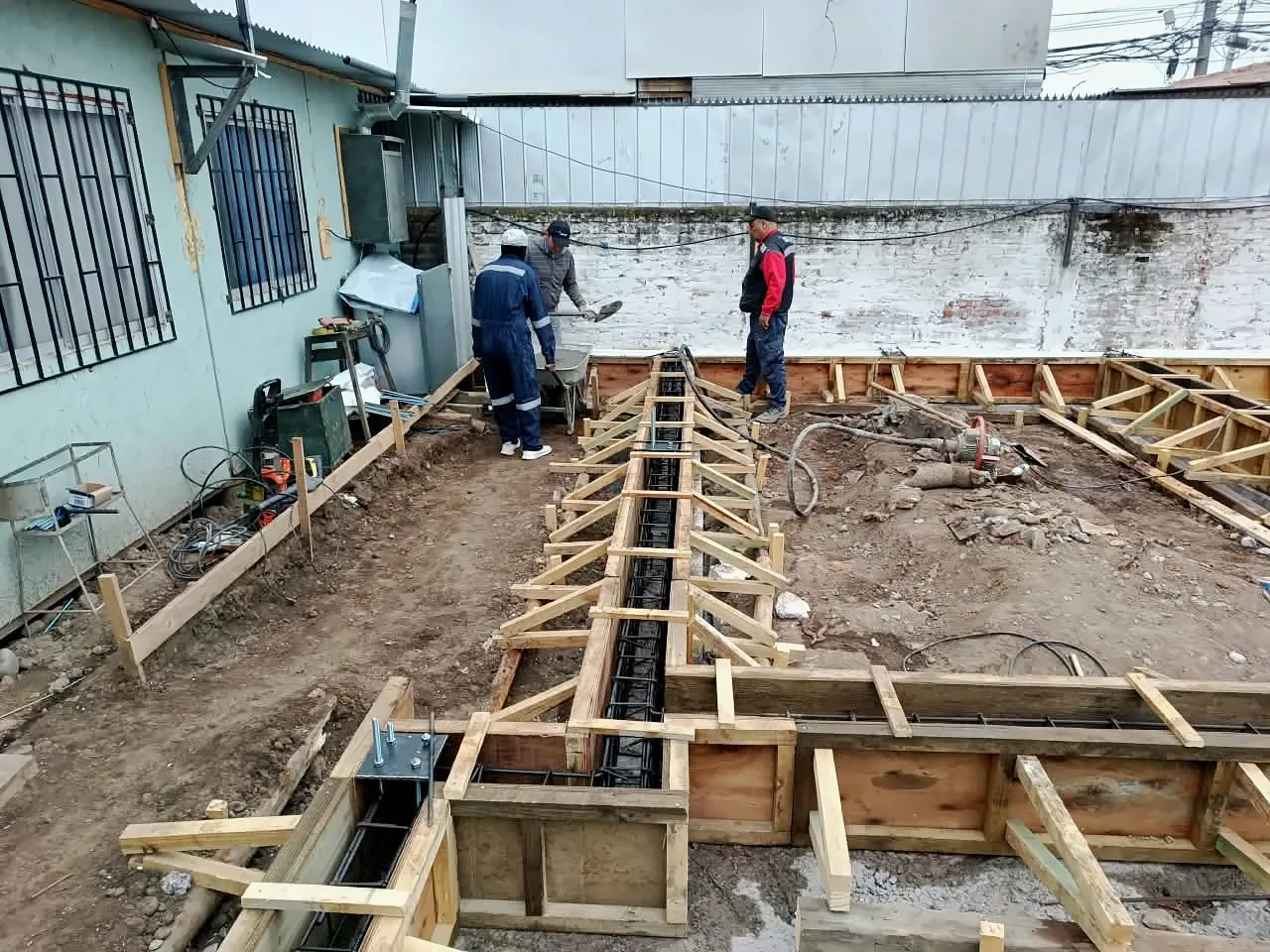 Equipo de Núcleo Construcción armando moldajes y enfierradura de una fundación junto a una casa